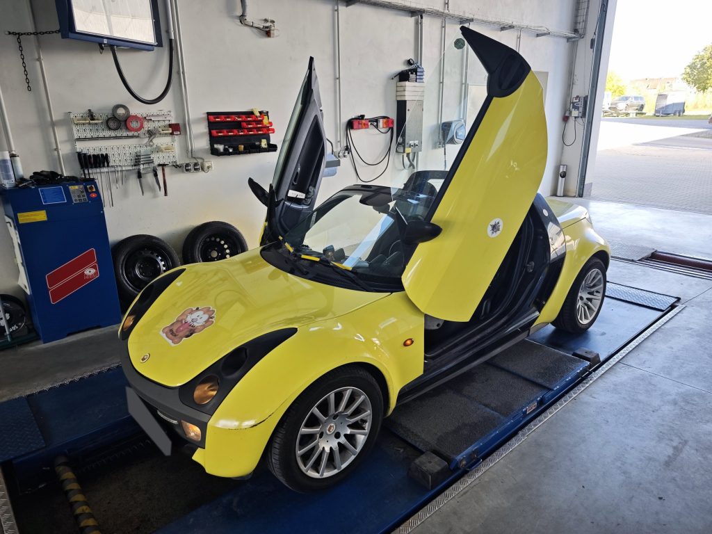 Gelber Smart Roadster mit nach oben geöffneten Flügeltüren auf dem Prüfstand